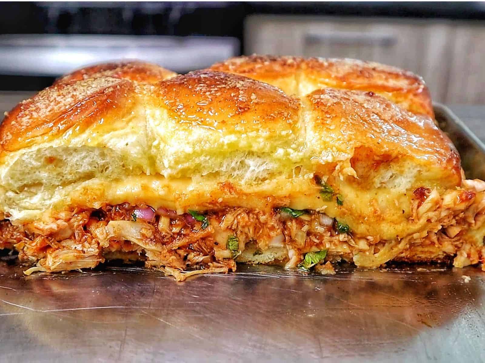 Baked BBQ chicken sliders made with Hawaiian rolls, shredded BBQ chicken, melted Gouda cheese, diced red onion, and cilantro, brushed with garlic herb butter.