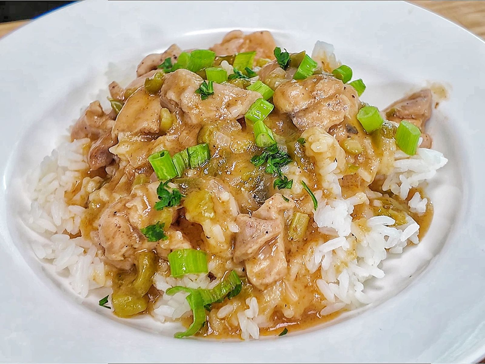 A bowl of homemade Chicken Étouffée served over fluffy white rice, with tender Cajun-seasoned chicken in a rich brown gravy with onions, celery, bell peppers, and topped with fresh green onions and parsley.
