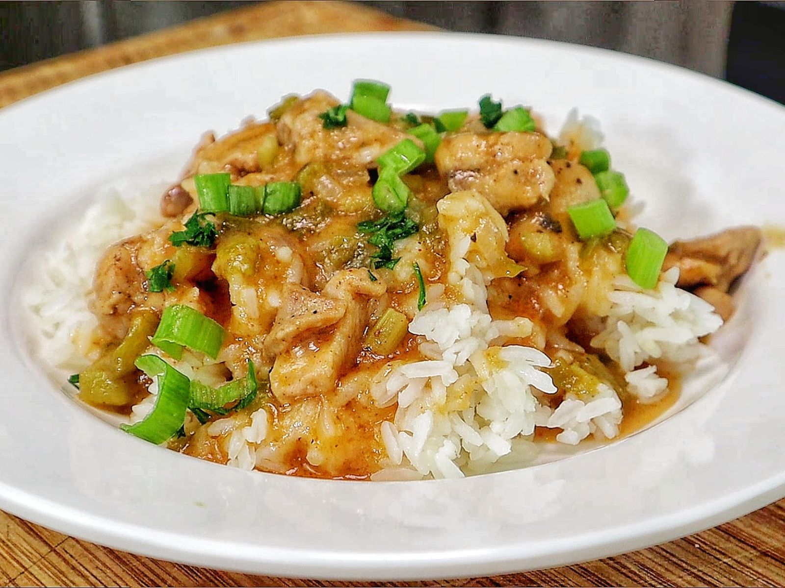 A bowl of homemade Chicken Étouffée served over fluffy white rice, with tender Cajun-seasoned chicken in a rich brown gravy with onions, celery, bell peppers, and topped with fresh green onions and parsley.