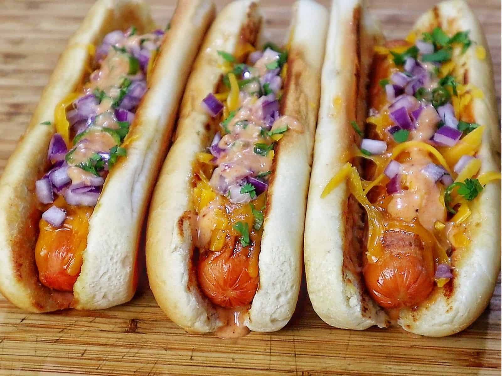 grilled hot dogs in toasted buns topped with melted sharp cheddar cheese, diced red onions, fresh cilantro, jalapeños, and creamy spicy firecracker sauce.