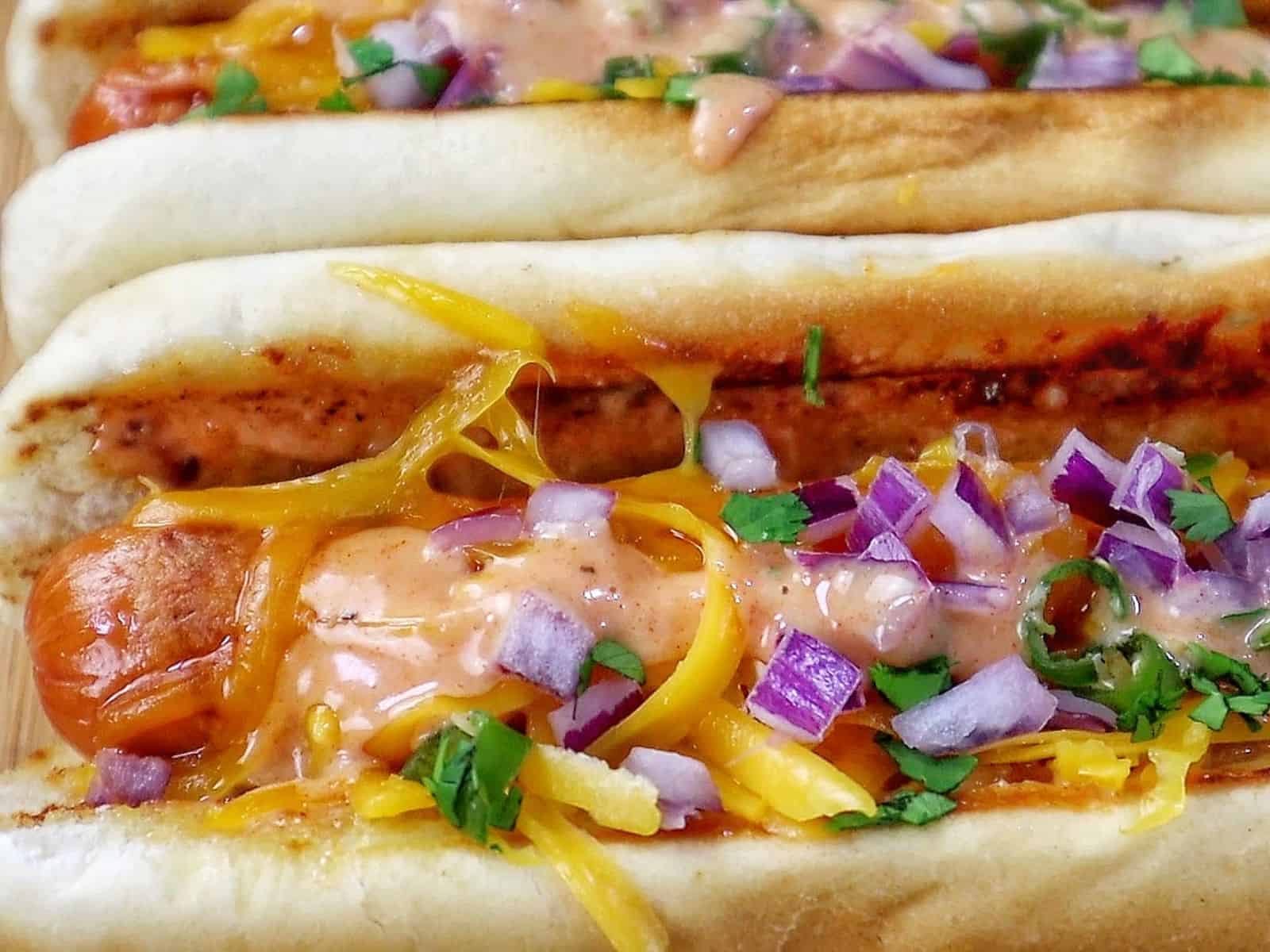 grilled hot dogs in toasted buns topped with melted sharp cheddar cheese, diced red onions, fresh cilantro, jalapeños, and creamy spicy firecracker sauce.