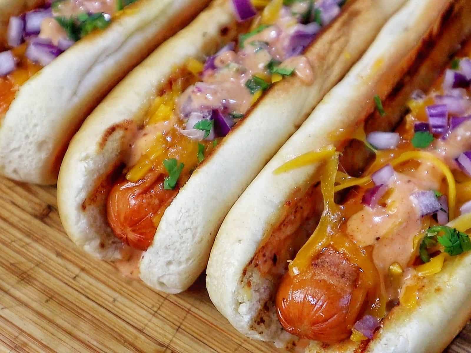 grilled hot dogs in toasted buns topped with melted sharp cheddar cheese, diced red onions, fresh cilantro, jalapeños, and creamy spicy firecracker sauce.