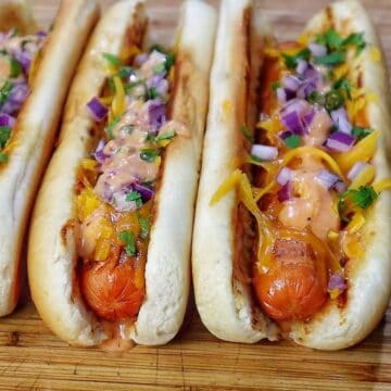 grilled hot dogs in toasted buns topped with melted sharp cheddar cheese, diced red onions, fresh cilantro, jalapeños, and creamy spicy firecracker sauce.