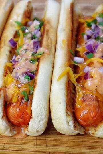 grilled hot dogs in toasted buns topped with melted sharp cheddar cheese, diced red onions, fresh cilantro, jalapeños, and creamy spicy firecracker sauce.