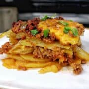 A cheesy Taco Potato Bake made with layers of seasoned ground beef, tender sliced potatoes, salsa, melted Mexican cheese, and topped with fresh green onions and sour cream.