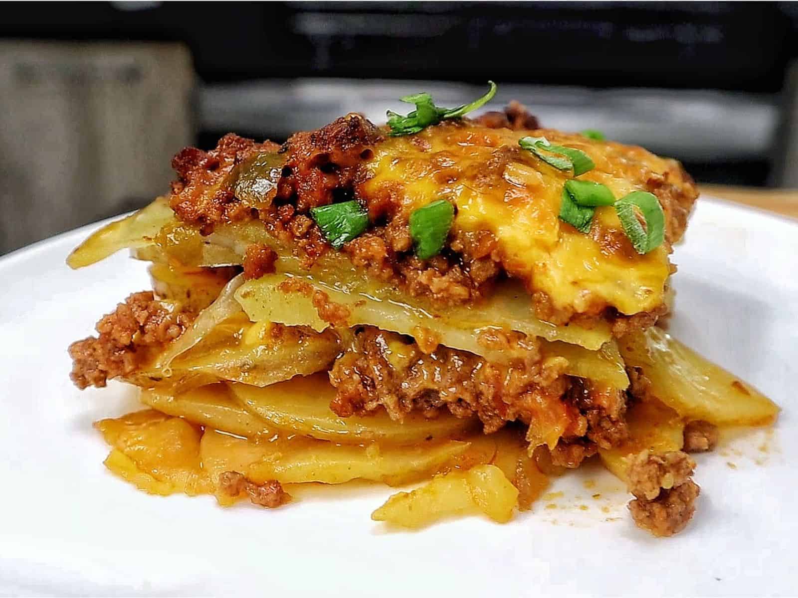 A cheesy Taco Potato Bake made with layers of seasoned ground beef, tender sliced potatoes, salsa, melted Mexican cheese, and topped with fresh green onions and sour cream.