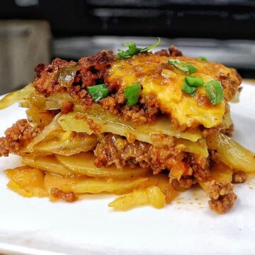 A cheesy Taco Potato Bake made with layers of seasoned ground beef, tender sliced potatoes, salsa, melted Mexican cheese, and topped with fresh green onions and sour cream.