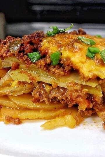 A cheesy Taco Potato Bake made with layers of seasoned ground beef, tender sliced potatoes, salsa, melted Mexican cheese, and topped with fresh green onions and sour cream.