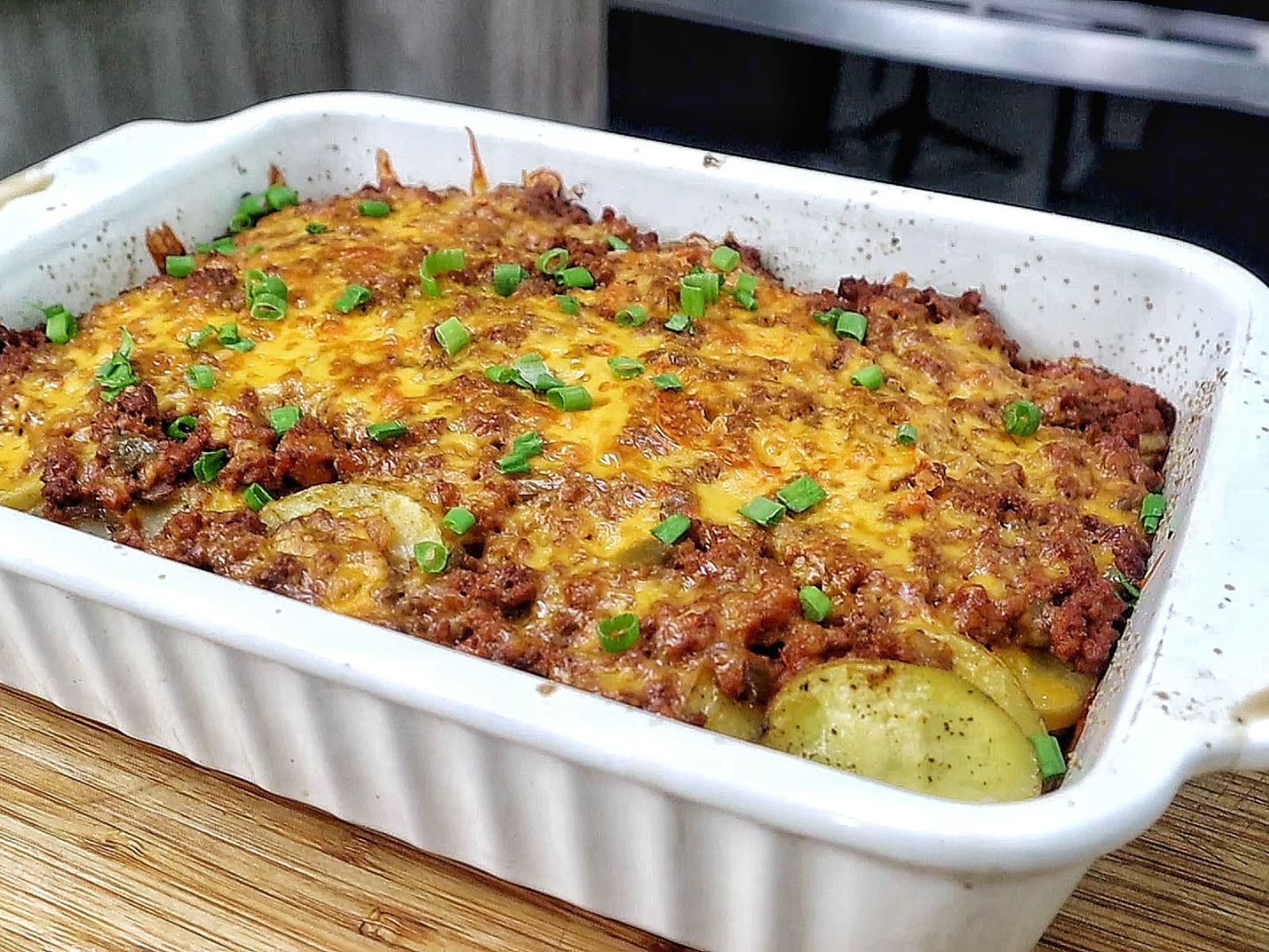 A cheesy Taco Potato Bake made with layers of seasoned ground beef, tender sliced potatoes, salsa, melted Mexican cheese, and topped with fresh green onions and sour cream.