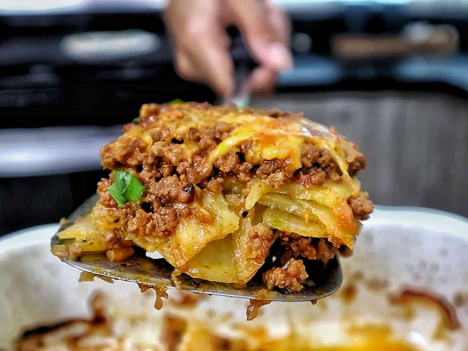 A cheesy Taco Potato Bake made with layers of seasoned ground beef, tender sliced potatoes, salsa, melted Mexican cheese, and topped with fresh green onions and sour cream.