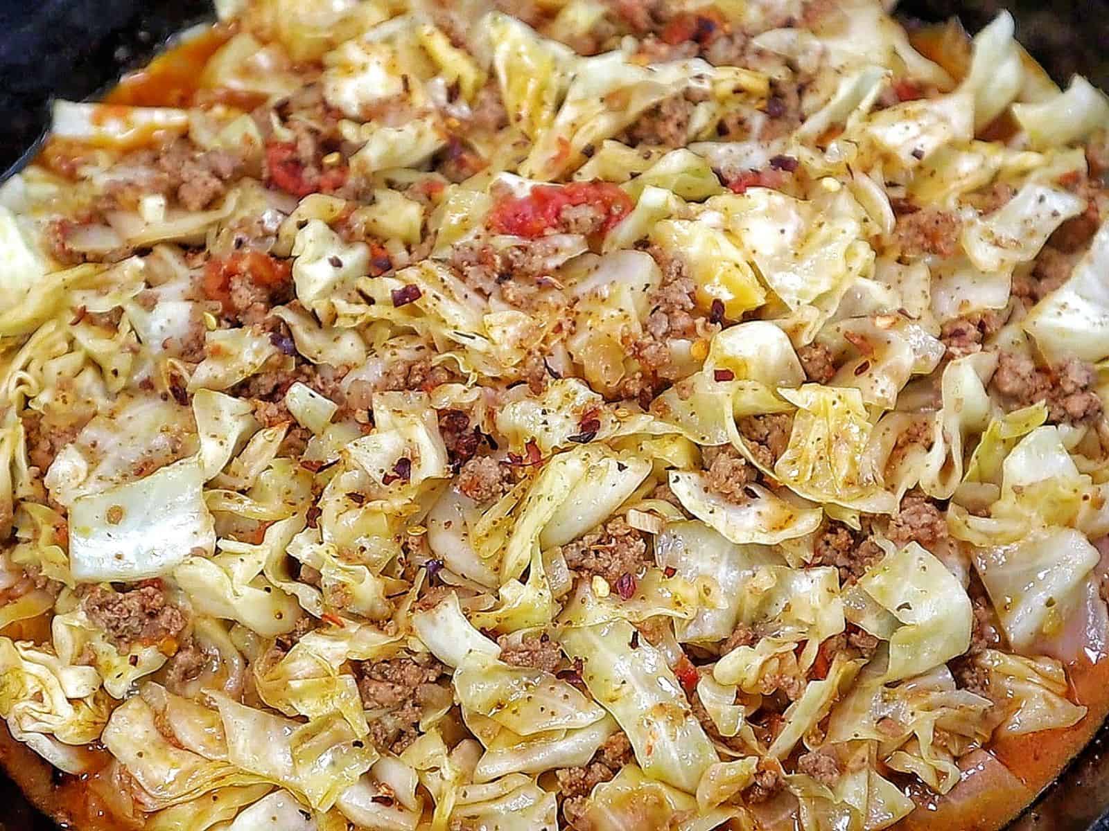 Ground beef and chopped cabbage cooked together in a cast-iron skillet with diced tomatoes, onions, garlic, and seasonings, finished with red pepper flakes for an easy one-pan dinner.