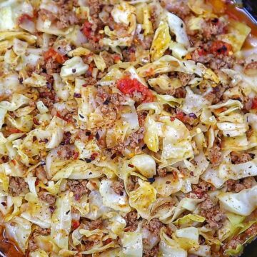 Ground beef and chopped cabbage cooked together in a cast-iron skillet with diced tomatoes, onions, garlic, and seasonings, finished with red pepper flakes for an easy one-pan dinner.