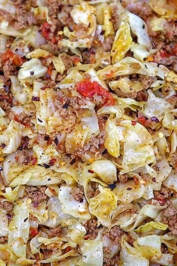Ground beef and chopped cabbage cooked together in a cast-iron skillet with diced tomatoes, onions, garlic, and seasonings, finished with red pepper flakes for an easy one-pan dinner.