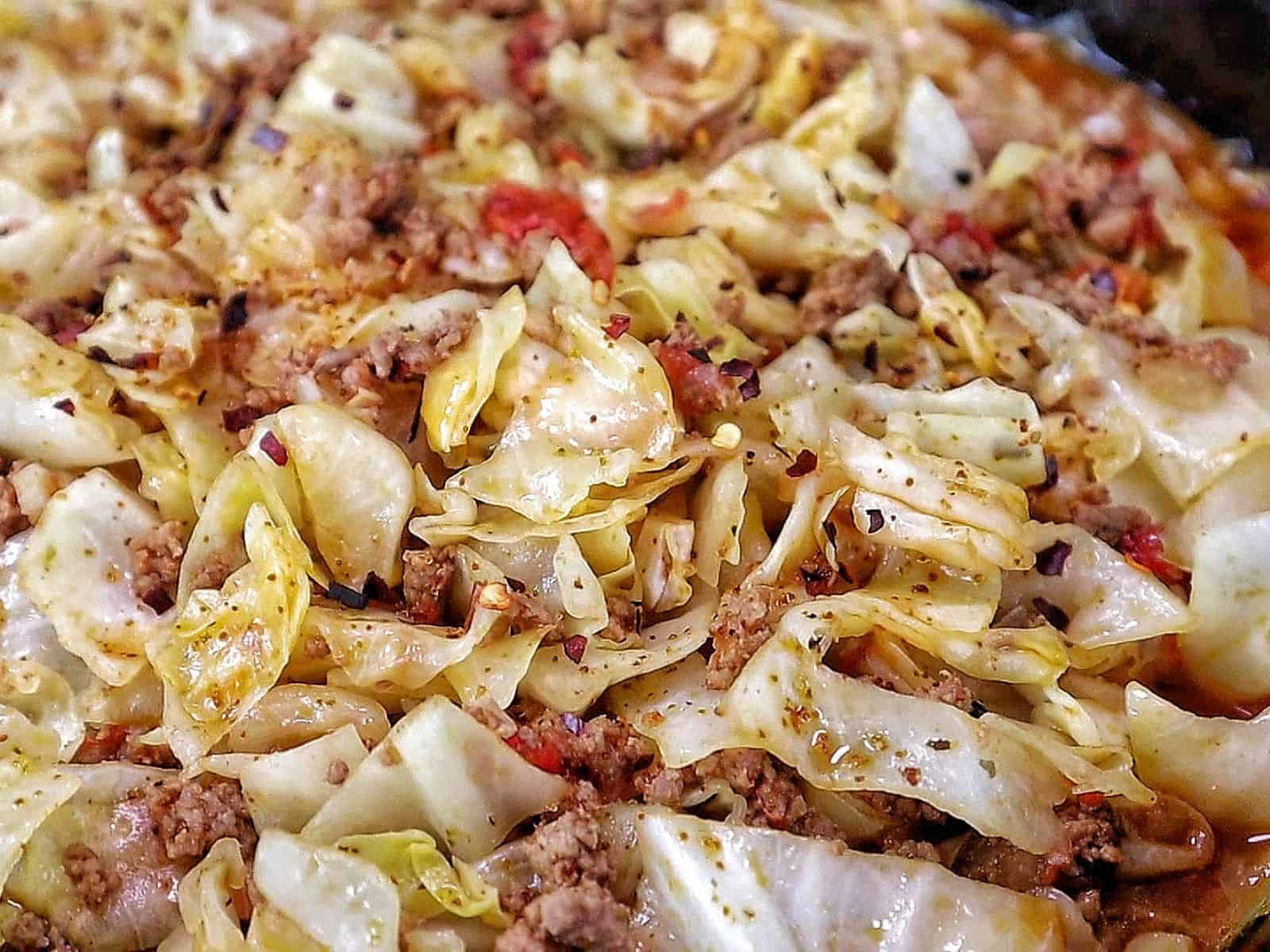 Ground beef and chopped cabbage cooked together in a cast-iron skillet with diced tomatoes, onions, garlic, and seasonings, finished with red pepper flakes for an easy one-pan dinner.