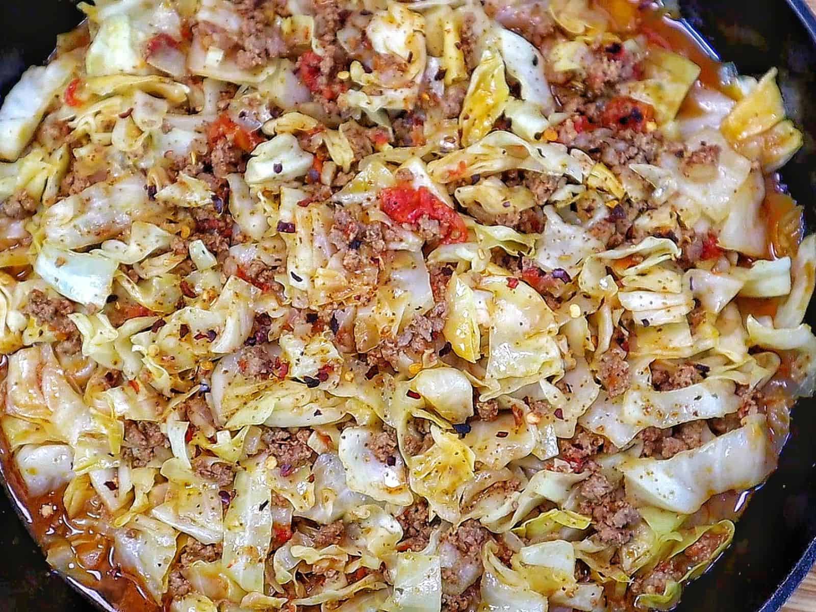 Ground beef and chopped cabbage cooked together in a cast-iron skillet with diced tomatoes, onions, garlic, and seasonings, finished with red pepper flakes for an easy one-pan dinner.