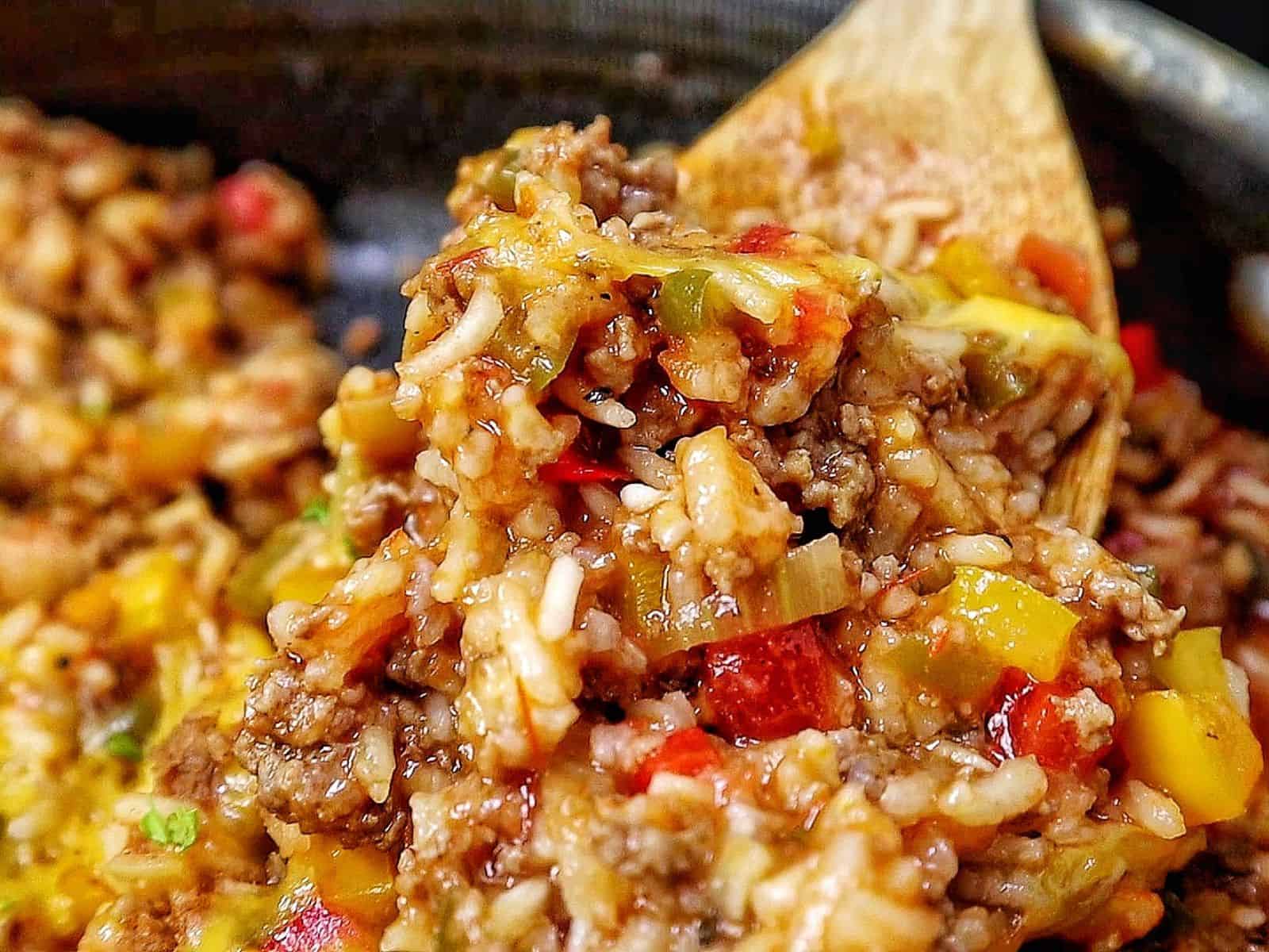 Cheesy unstuffed bell pepper skillet made with seasoned ground beef, white rice, red, yellow and green bell peppers, tomatoes and melted cheddar cheese, garnished with fresh parsley.