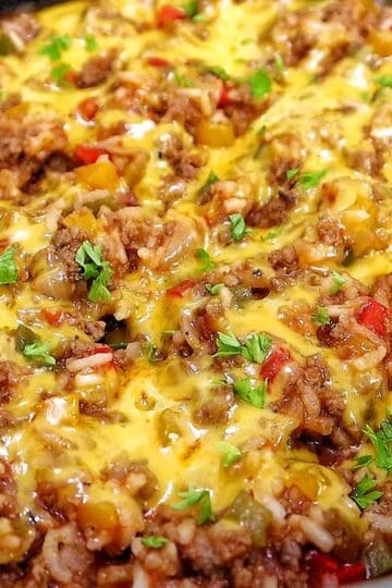 Cheesy unstuffed bell pepper skillet made with seasoned ground beef, white rice, red, yellow and green bell peppers, tomatoes and melted cheddar cheese, garnished with fresh parsley.