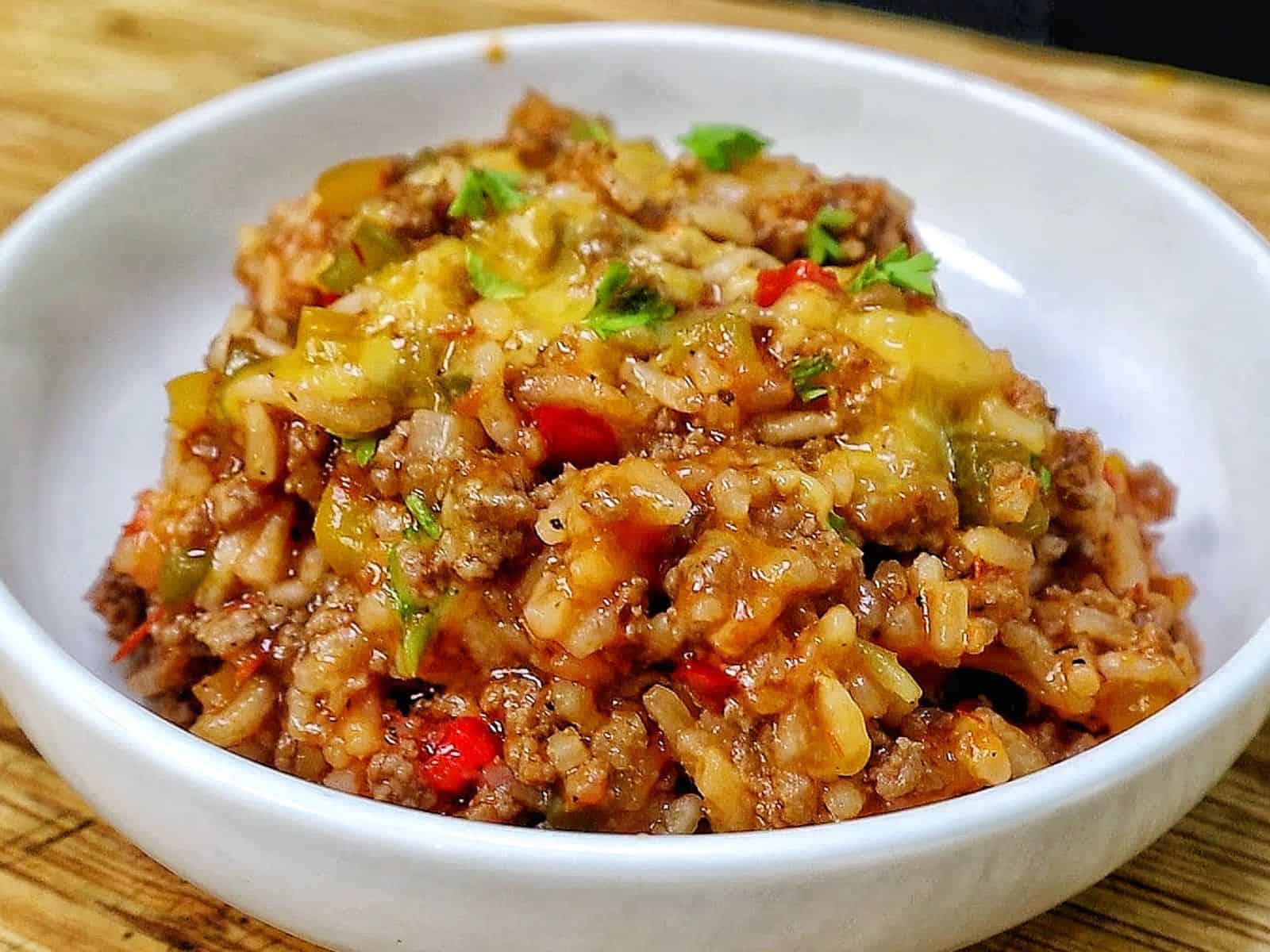 Cheesy unstuffed bell pepper skillet made with seasoned ground beef, white rice, red, yellow and green bell peppers, tomatoes and melted cheddar cheese, garnished with fresh parsley.