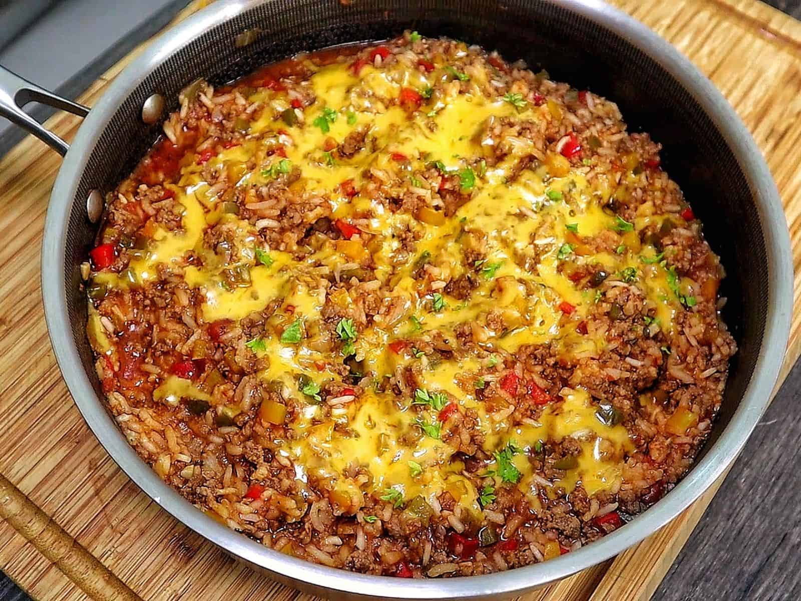 Cheesy unstuffed bell pepper skillet made with seasoned ground beef, white rice, red, yellow and green bell peppers, tomatoes and melted cheddar cheese, garnished with fresh parsley.