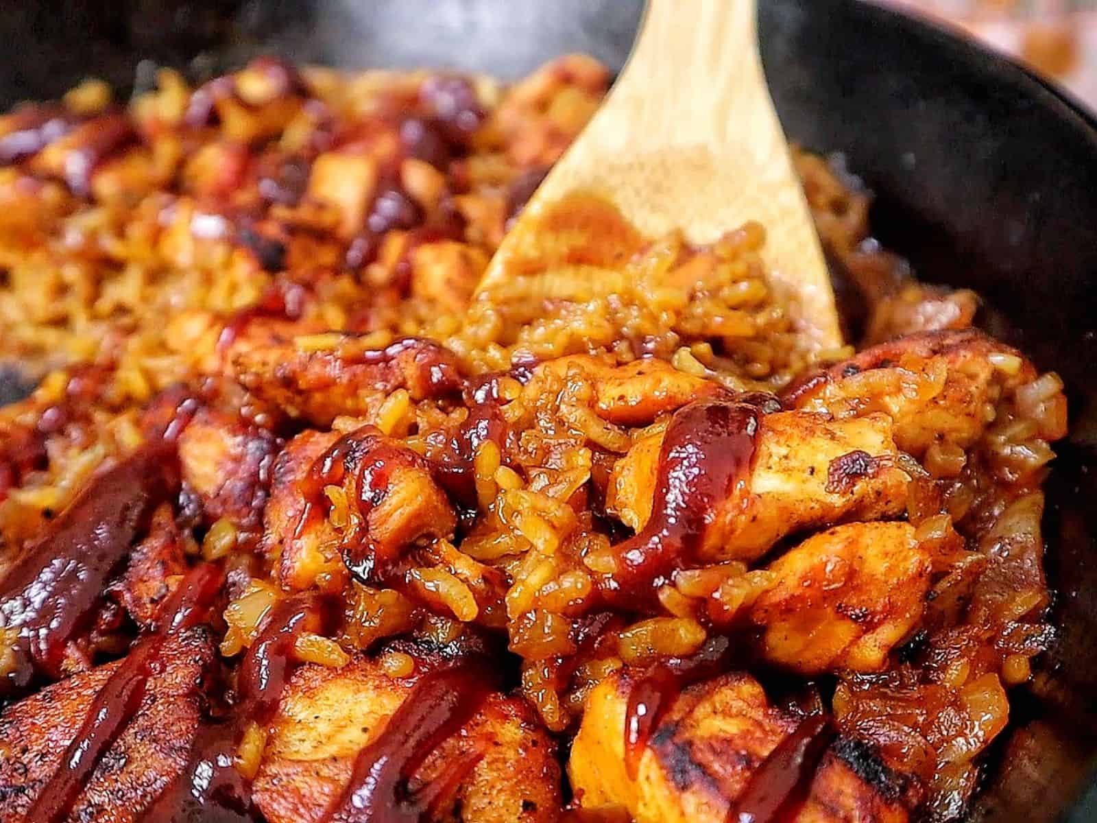 Honey BBQ chicken and rice cooked in a skillet, featuring tender chunks of seasoned chicken, fluffy rice, caramelized onions, and a glossy drizzle of rich barbecue sauce.