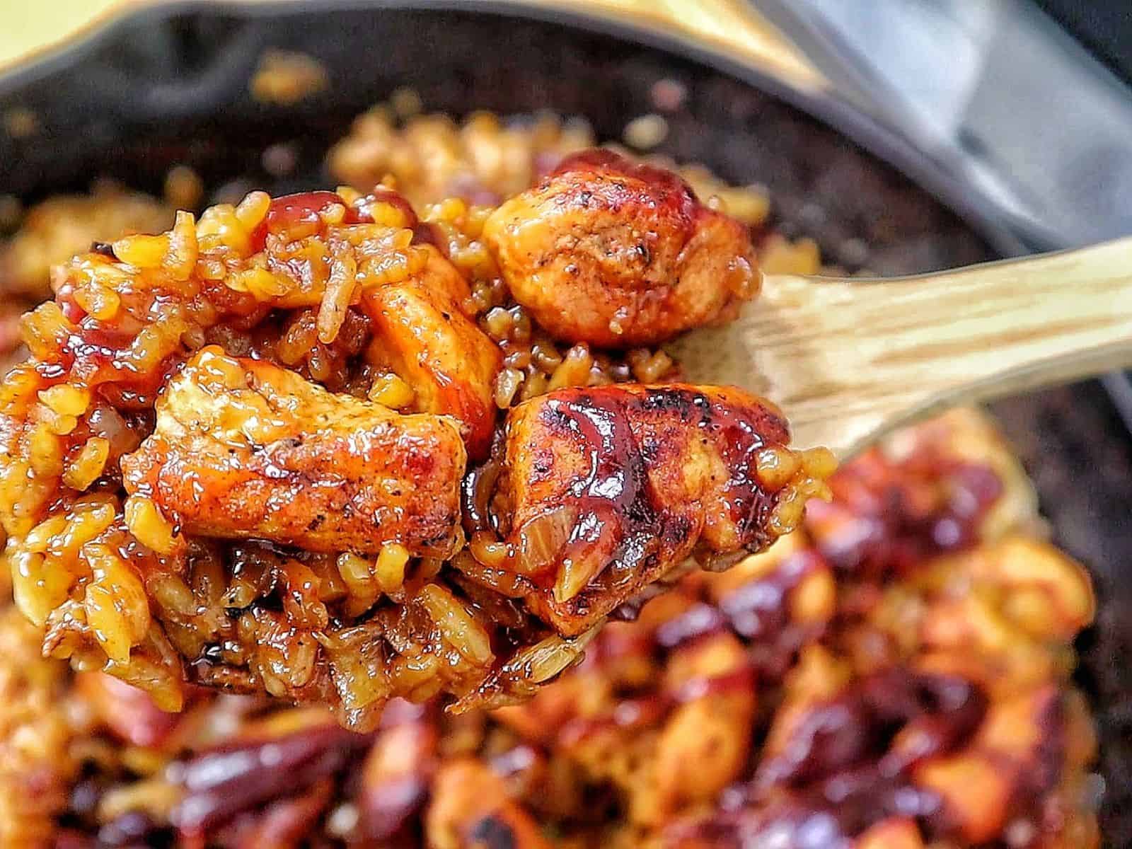 Honey BBQ chicken and rice cooked in a skillet, featuring tender chunks of seasoned chicken, fluffy rice, caramelized onions, and a glossy drizzle of rich barbecue sauce.