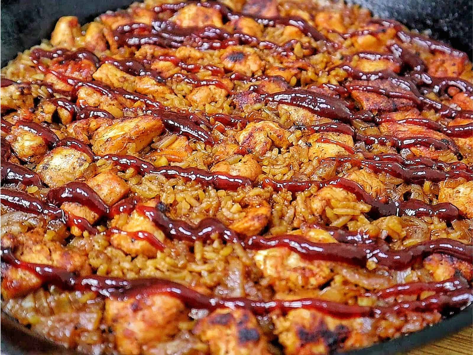Honey BBQ chicken and rice cooked in a skillet, featuring tender chunks of seasoned chicken, fluffy rice, caramelized onions, and a glossy drizzle of rich barbecue sauce.