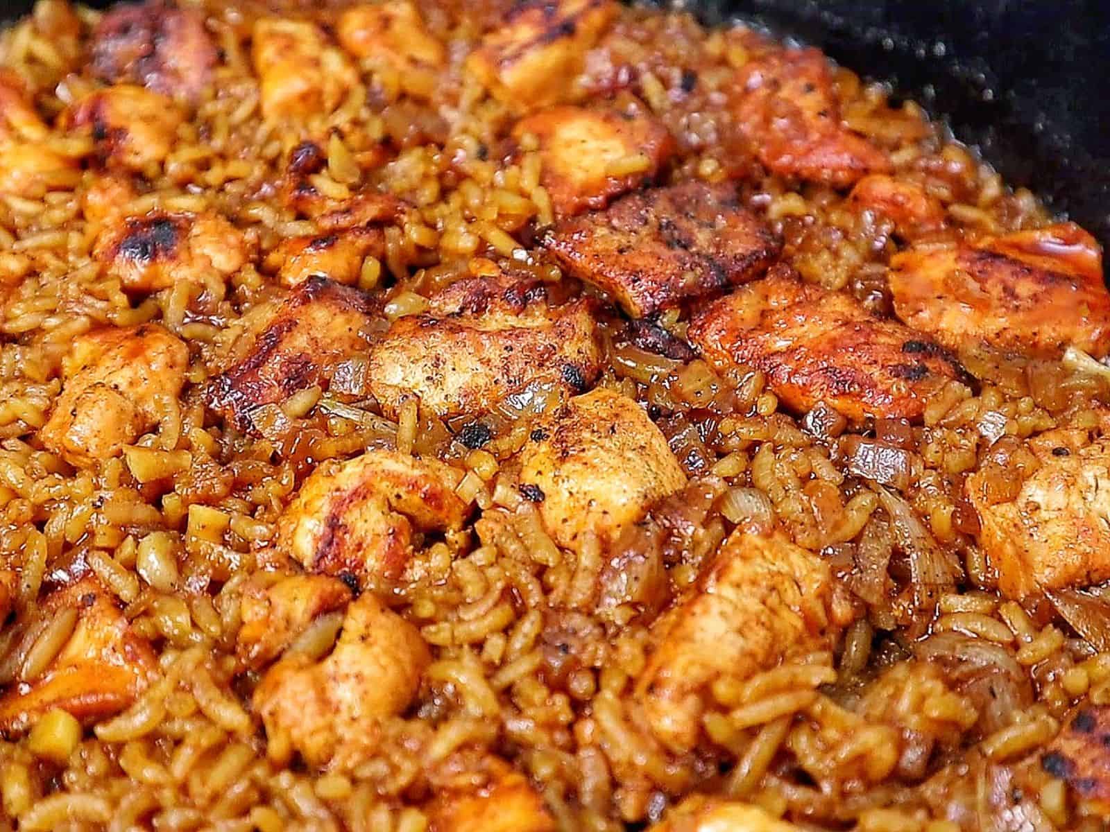 Honey BBQ chicken and rice cooked in a skillet, featuring tender chunks of seasoned chicken, fluffy rice, caramelized onions, and a glossy drizzle of rich barbecue sauce.