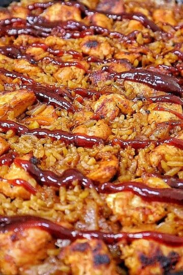 Honey BBQ chicken and rice cooked in a skillet, featuring tender chunks of seasoned chicken, fluffy rice, caramelized onions, and a glossy drizzle of rich barbecue sauce.