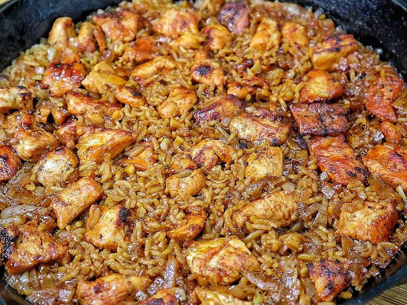 Honey BBQ chicken and rice cooked in a skillet, featuring tender chunks of seasoned chicken, fluffy rice, caramelized onions, and a glossy drizzle of rich barbecue sauce.