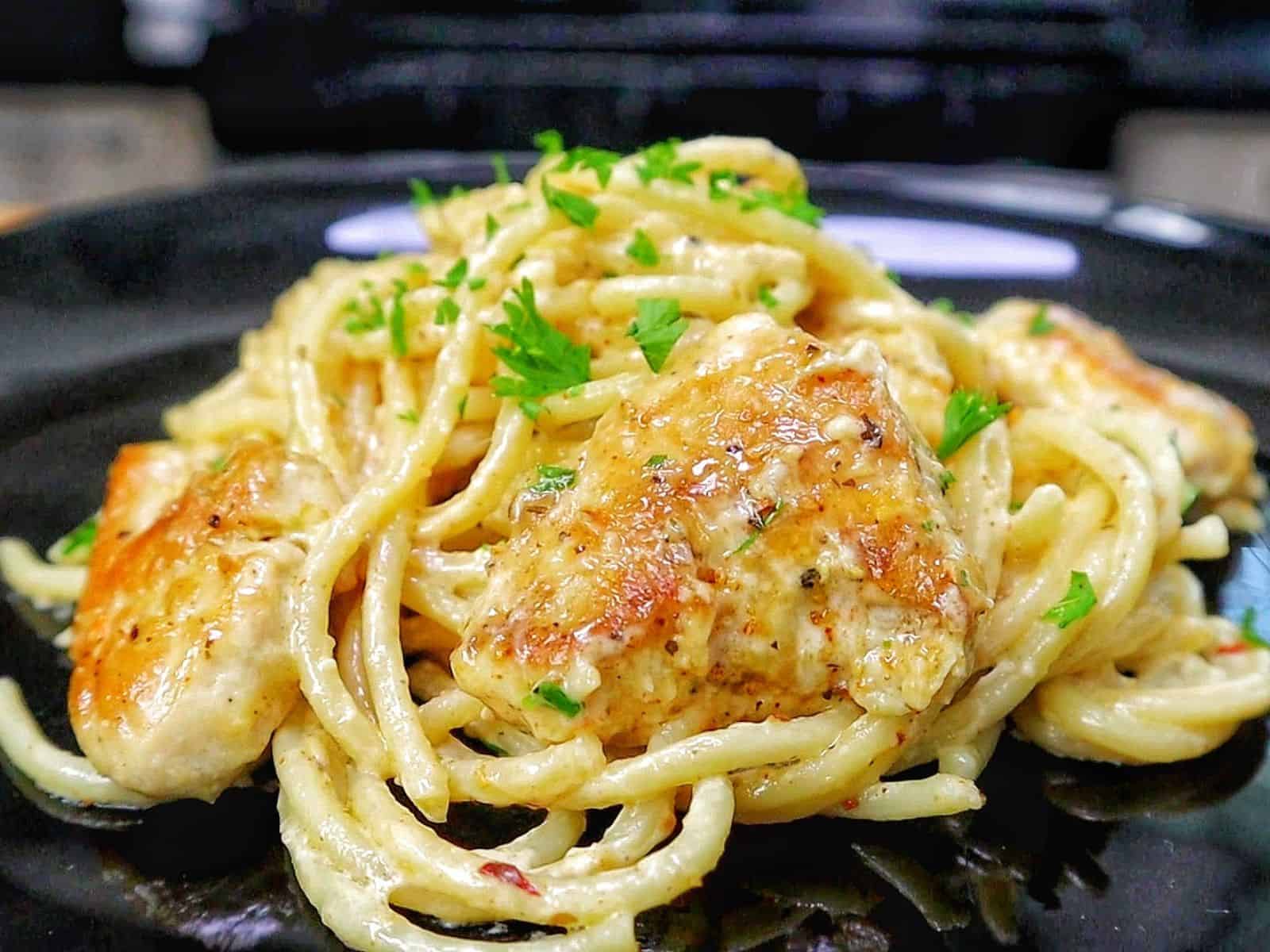 Three Cheese Chicken Spaghetti made with tender golden chicken breast, spaghetti coated in a rich Cajun garlic Parmesan cream sauce, and topped with fresh parsley.