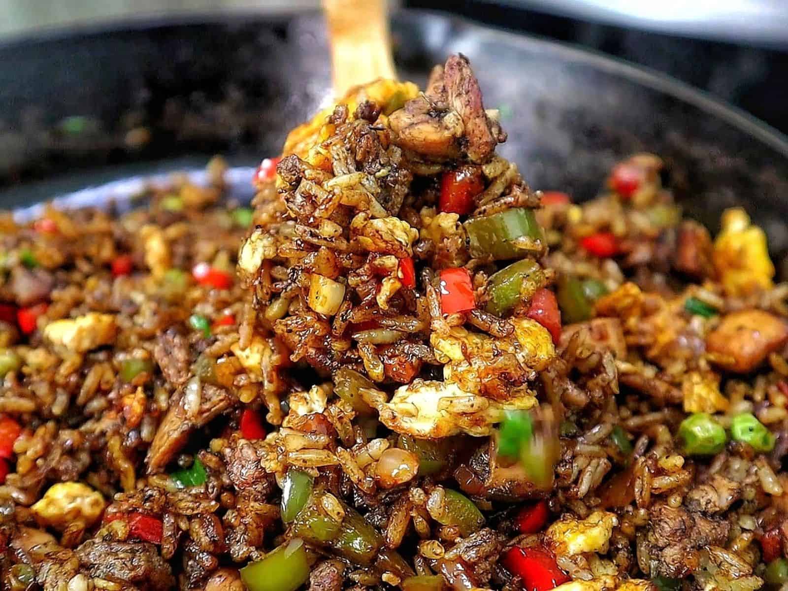 Homemade Jerk Chicken Fried Rice loaded with seasoned chicken thighs, fluffy rice, scrambled eggs, red and green bell peppers, peas and green onions in a savory jerk and soy sauce seasoning.