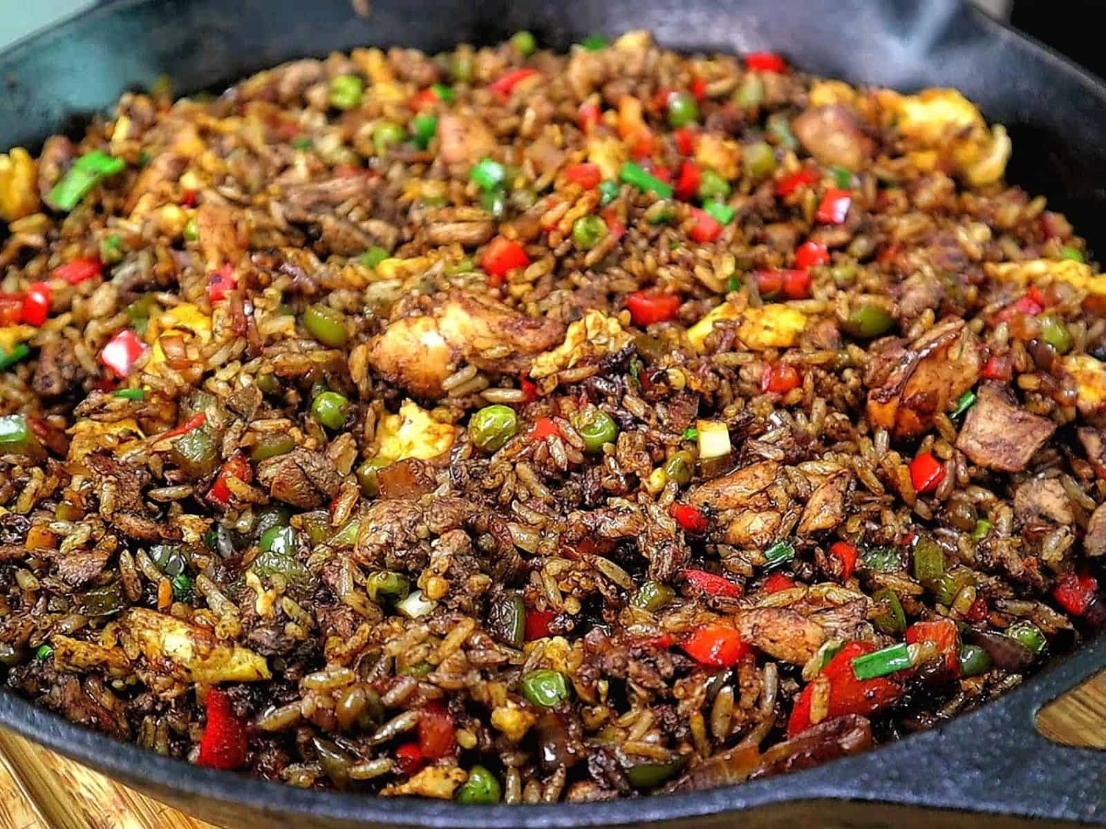 Homemade Jerk Chicken Fried Rice loaded with seasoned chicken thighs, fluffy rice, scrambled eggs, red and green bell peppers, peas and green onions in a savory jerk and soy sauce seasoning.