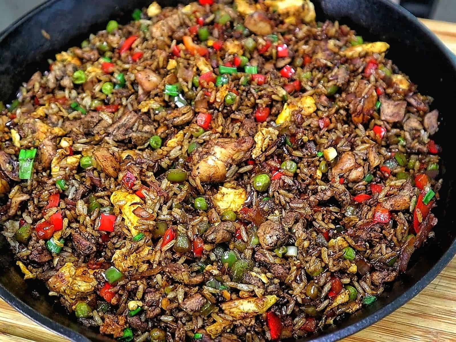 Homemade Jerk Chicken Fried Rice loaded with seasoned chicken thighs, fluffy rice, scrambled eggs, red and green bell peppers, peas and green onions in a savory jerk and soy sauce seasoning.