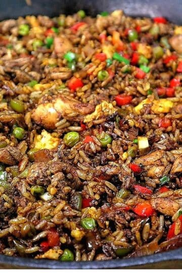 Homemade Jerk Chicken Fried Rice loaded with seasoned chicken thighs, fluffy rice, scrambled eggs, red and green bell peppers, peas and green onions in a savory jerk and soy sauce seasoning.