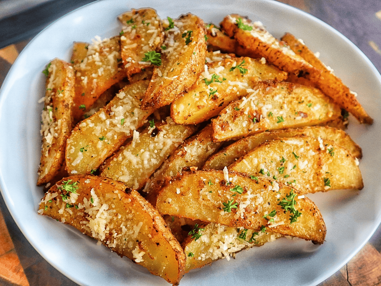 Golden-brown Garlic Parmesan Potato Wedges topped with freshly grated Parmesan cheese and chopped parsley, arranged on a wire rack over a baking sheet.