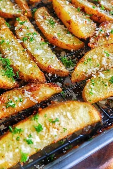Golden-brown Garlic Parmesan Potato Wedges topped with freshly grated Parmesan cheese and chopped parsley, arranged on a wire rack over a baking sheet.