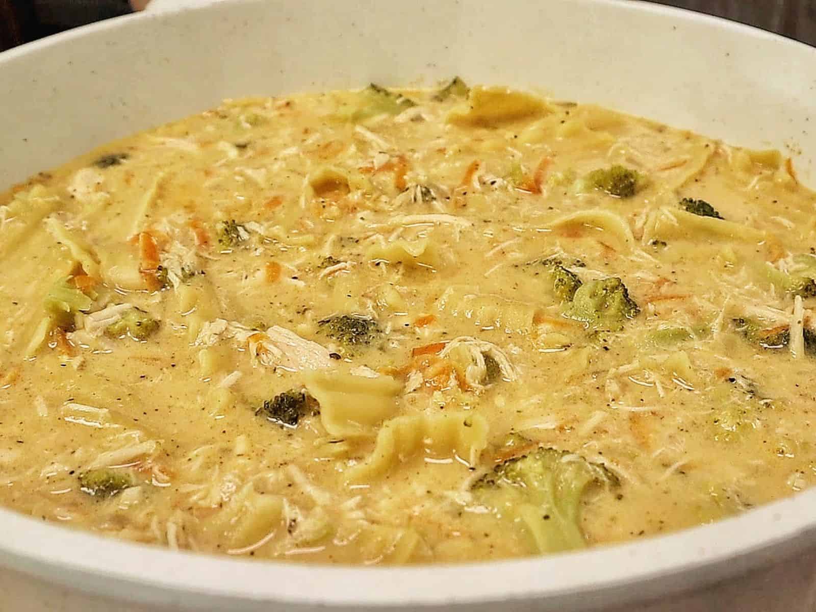 Creamy Broccoli Cheddar Lasagna Soup served in a white bowl with shredded chicken, tender lasagna noodles, broccoli florets and carrots in a rich cheddar cheese broth.