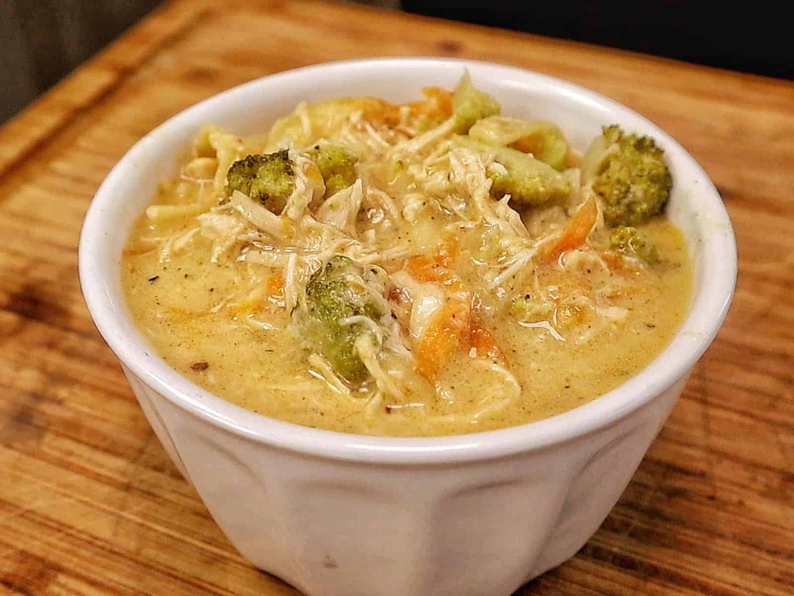 Creamy Broccoli Cheddar Lasagna Soup served in a white bowl with shredded chicken, tender lasagna noodles, broccoli florets and carrots in a rich cheddar cheese broth.