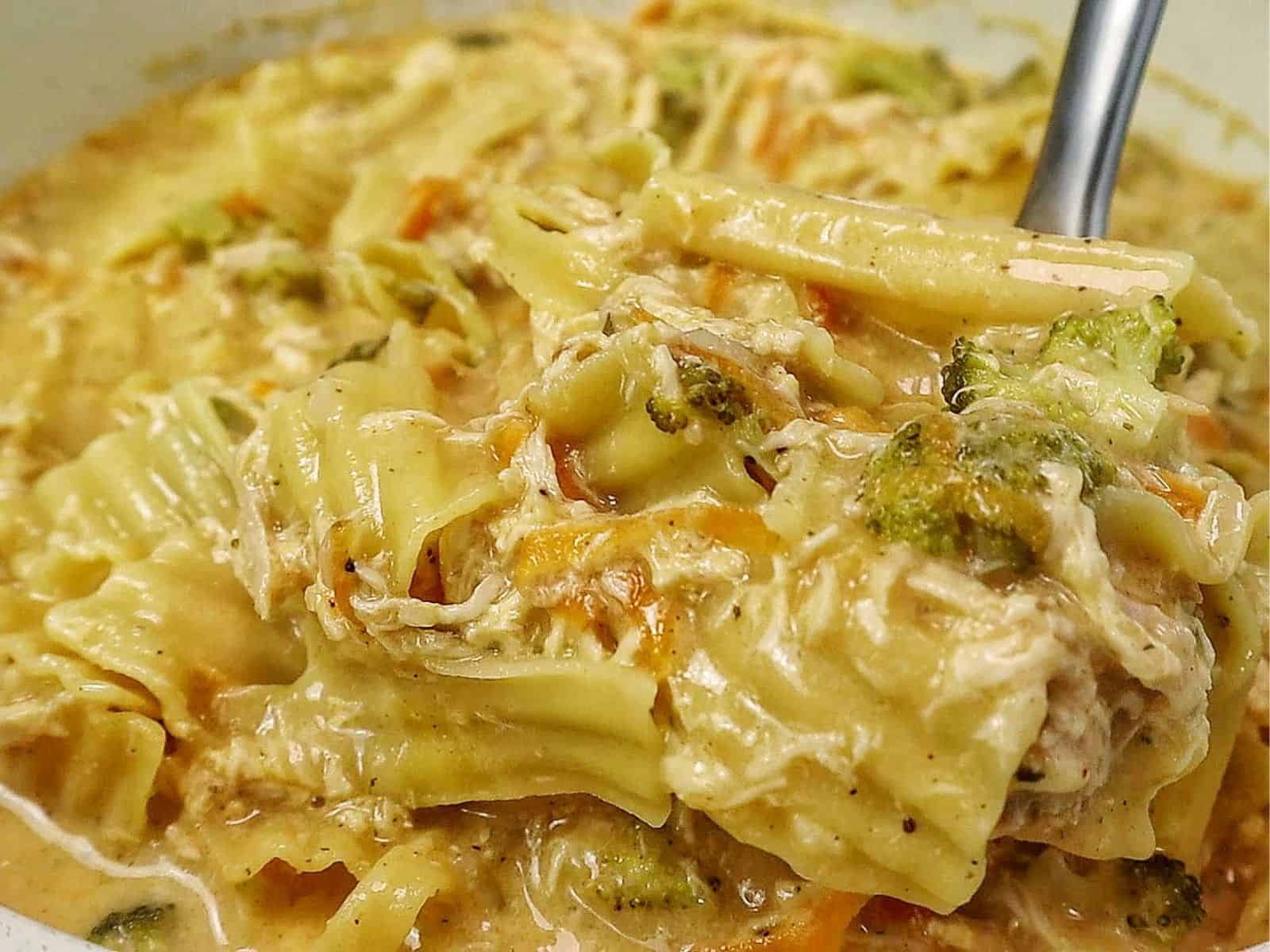 Creamy Broccoli Cheddar Lasagna Soup served in a white bowl with shredded chicken, tender lasagna noodles, broccoli florets and carrots in a rich cheddar cheese broth.