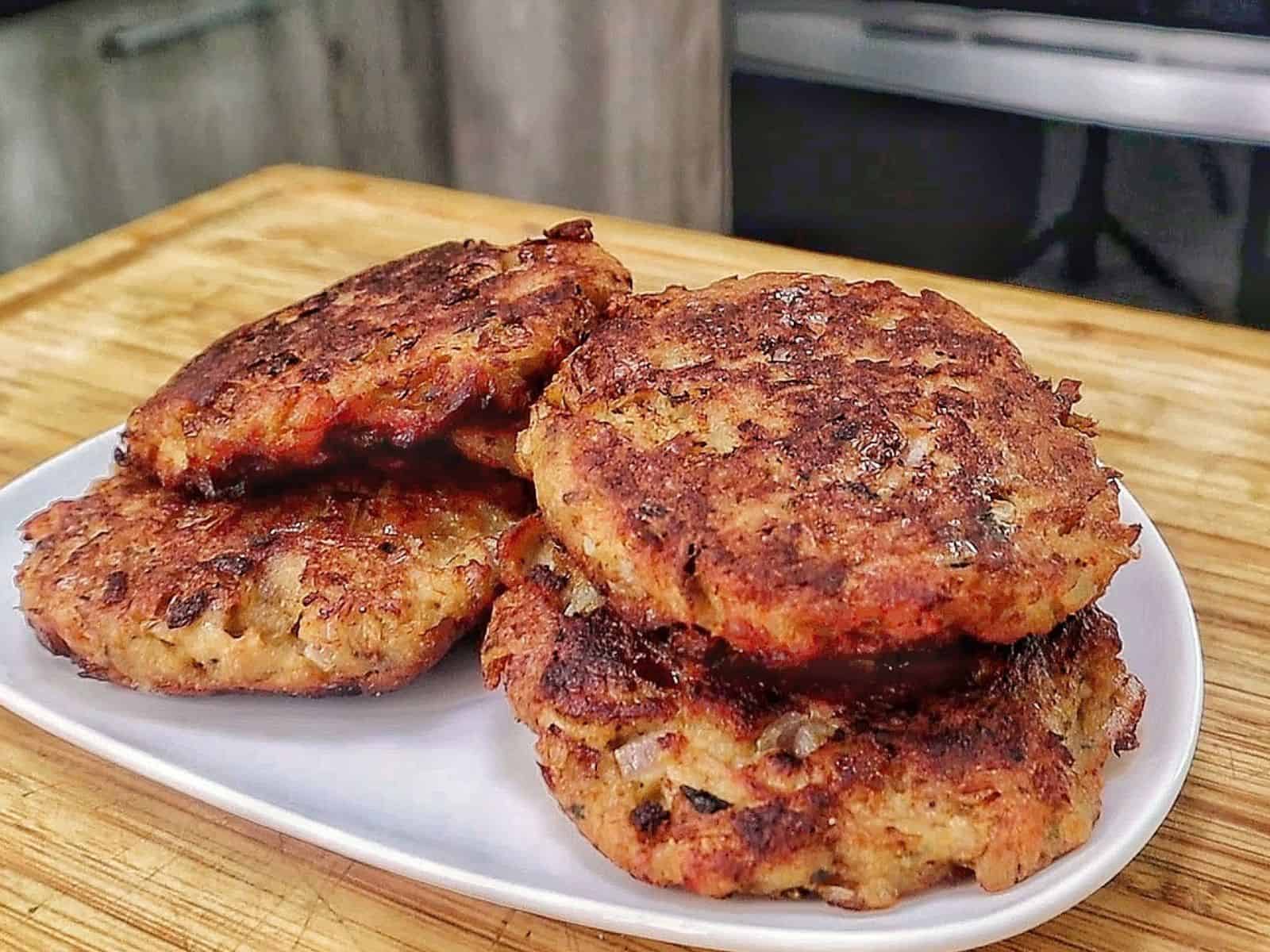 Crispy homemade tuna patties pan-fried until golden brown with chopped onions and herbs, stacked on a white plate.