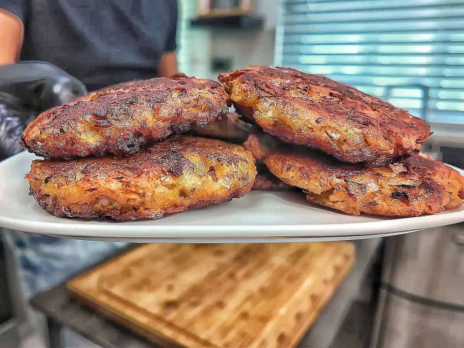 Crispy homemade tuna patties pan-fried until golden brown with chopped onions and herbs, stacked on a white plate.