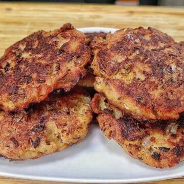 Crispy homemade tuna patties pan-fried until golden brown with chopped onions and herbs, stacked on a white plate.