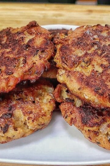 Crispy homemade tuna patties pan-fried until golden brown with chopped onions and herbs, stacked on a white plate.