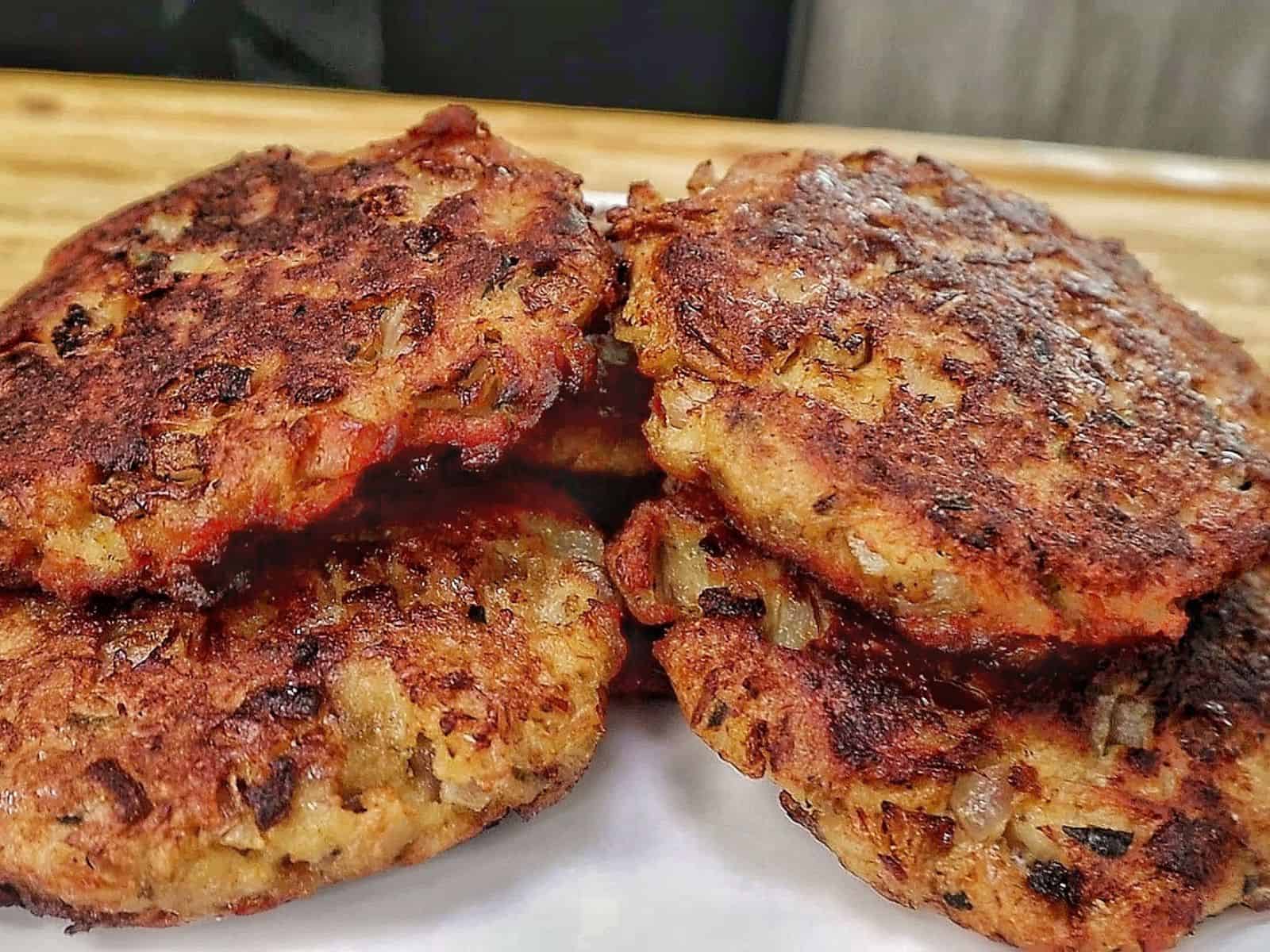 Crispy homemade tuna patties pan-fried until golden brown with chopped onions and herbs, stacked on a white plate.
