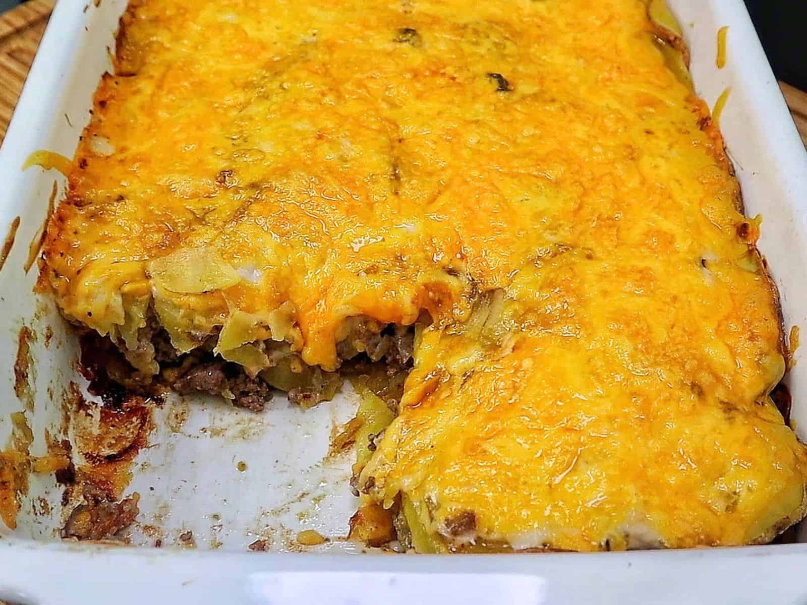 Homemade hamburger potato casserole layered with seasoned ground beef, tender sliced potatoes, creamy mushroom sauce and melted golden cheddar cheese in a white baking dish.