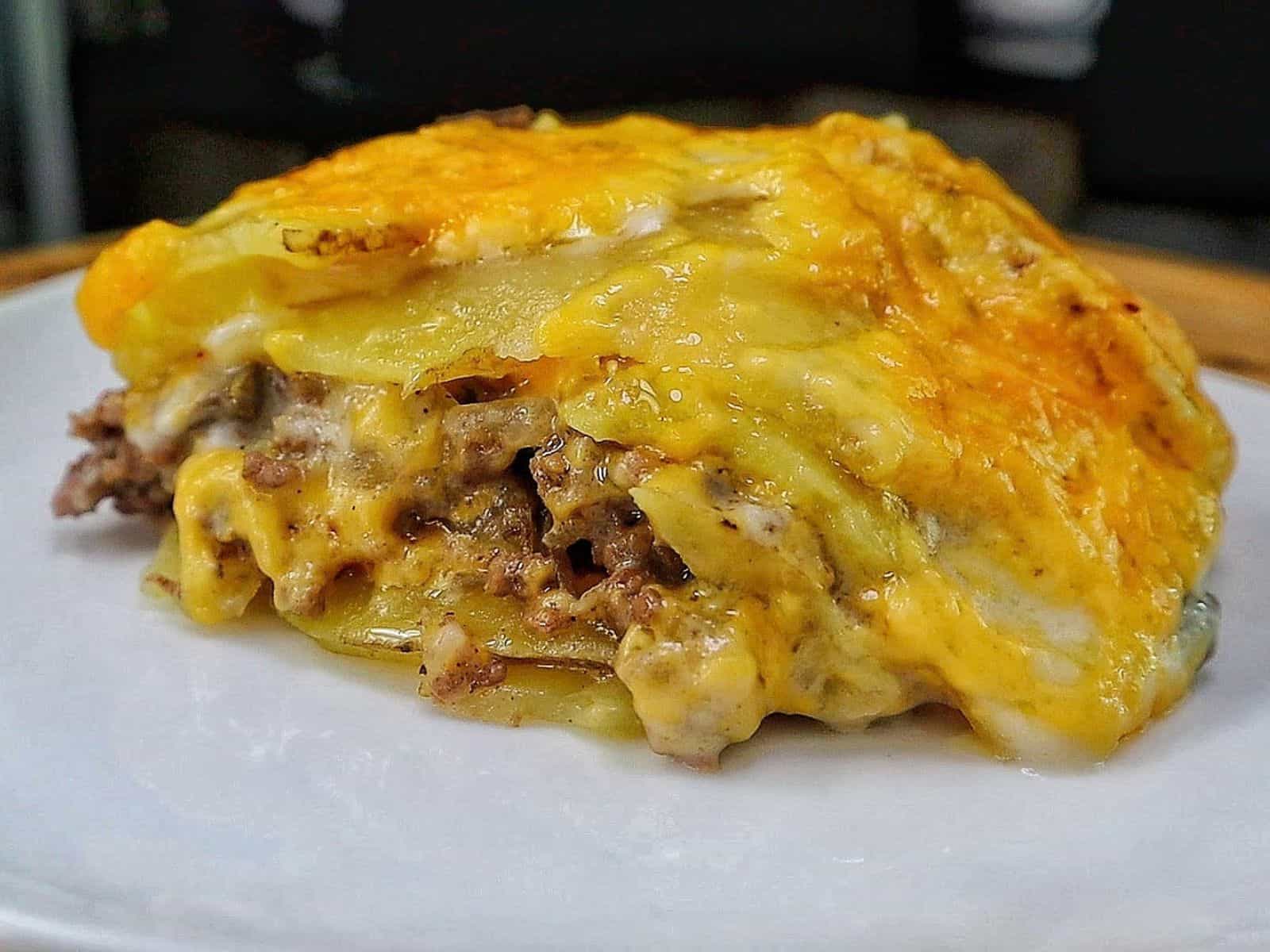 Homemade hamburger potato casserole layered with seasoned ground beef, tender sliced potatoes, creamy mushroom sauce and melted golden cheddar cheese in a white baking dish.