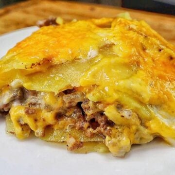 Homemade hamburger potato casserole layered with seasoned ground beef, tender sliced potatoes, creamy mushroom sauce and melted golden cheddar cheese in a white baking dish.