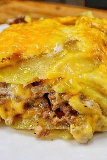 Homemade hamburger potato casserole layered with seasoned ground beef, tender sliced potatoes, creamy mushroom sauce and melted golden cheddar cheese in a white baking dish.