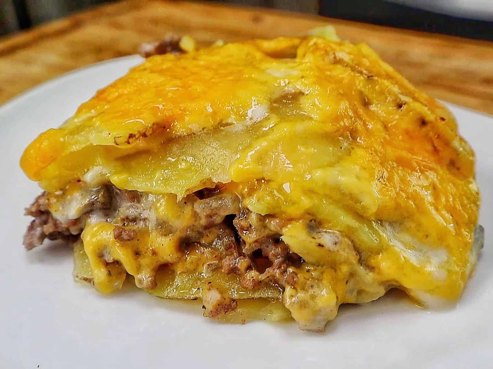 Homemade hamburger potato casserole layered with seasoned ground beef, tender sliced potatoes, creamy mushroom sauce and melted golden cheddar cheese in a white baking dish.
