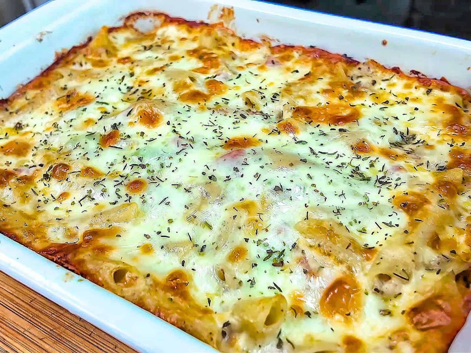 Homemade Italian Grinder Pasta Bake in a white casserole dish, topped with bubbly golden-brown melted cheese and sprinkled with Italian herbs.